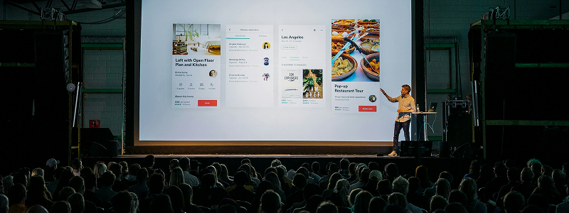 Presenter on stage with event screen and audience